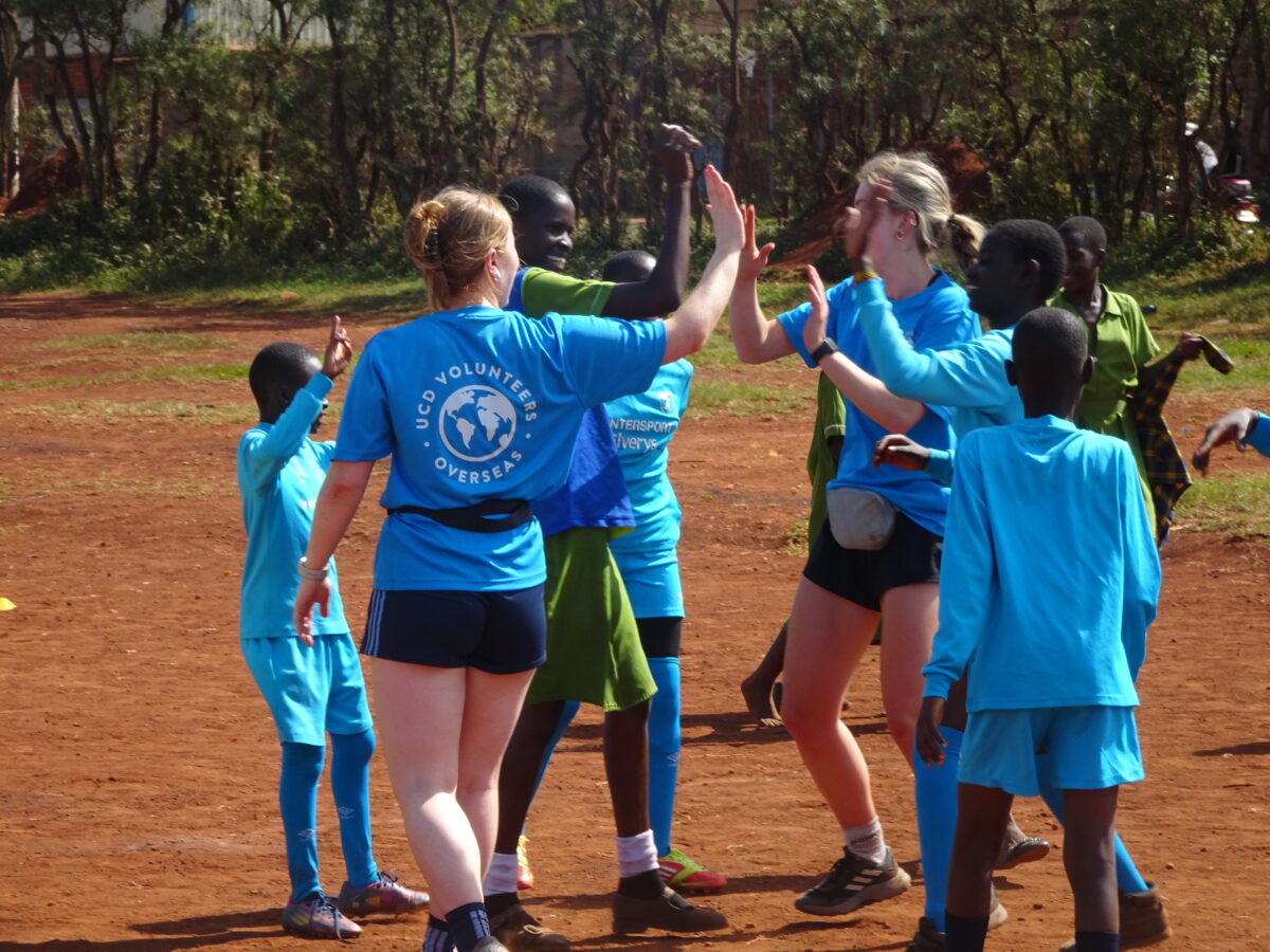 Two volunteers and three children high-five while playing Gaelic football. 