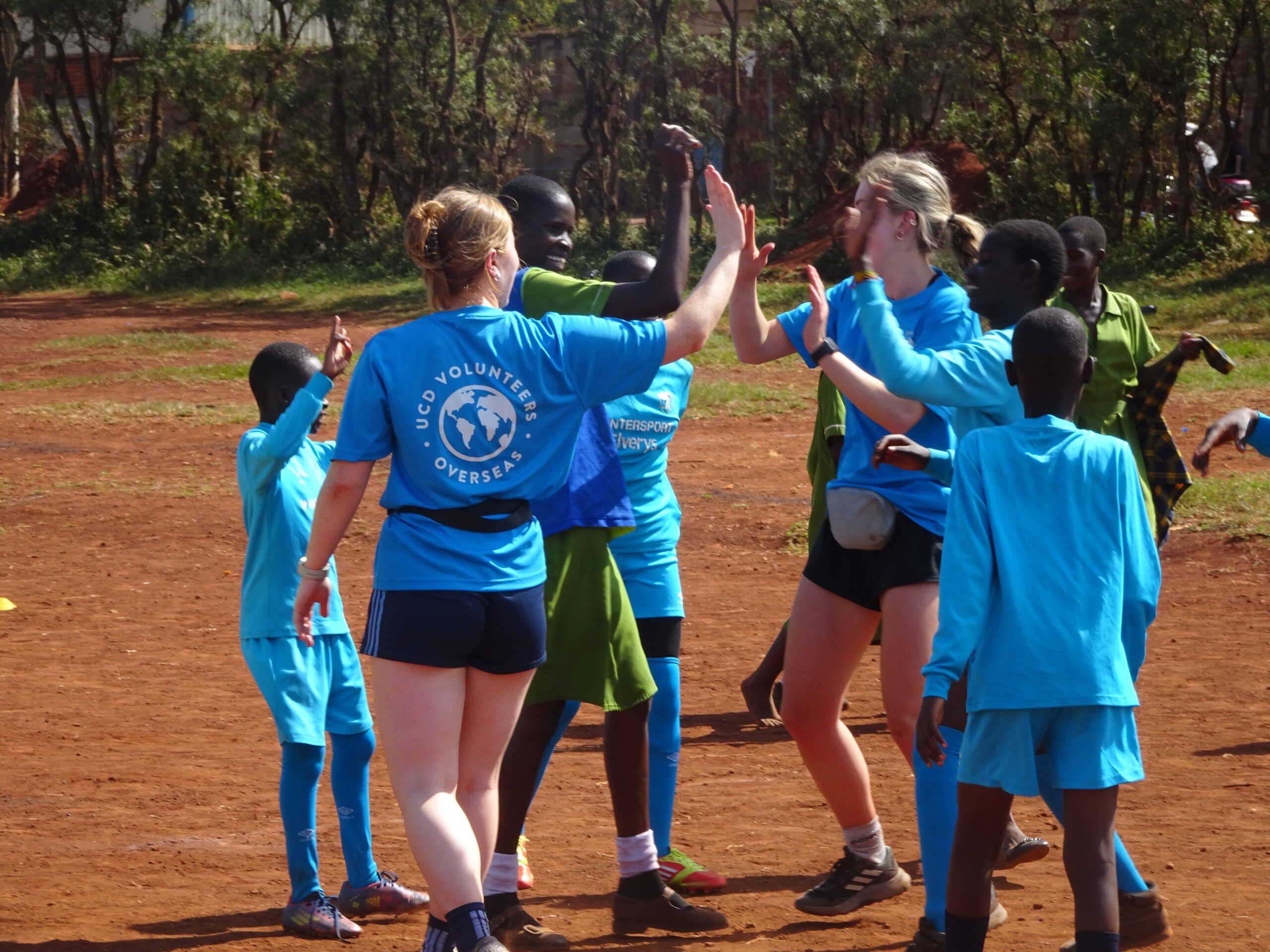 Two volunteers and three children high-five while playing Gaelic football.