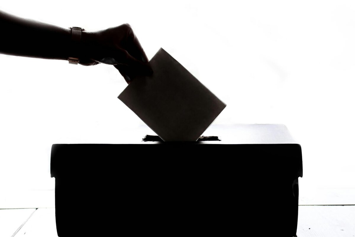 A hand places an envelope into a ballot box. 